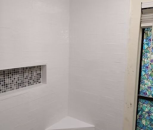 White tiled shower with built-in shelf lined with small mosaic tiles. Corner seat visible.