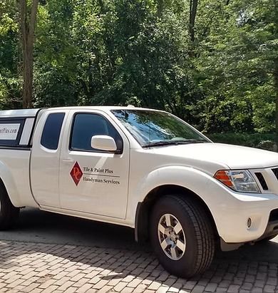 White Nissan pickup truck with company logo parked outside; trees in the background.