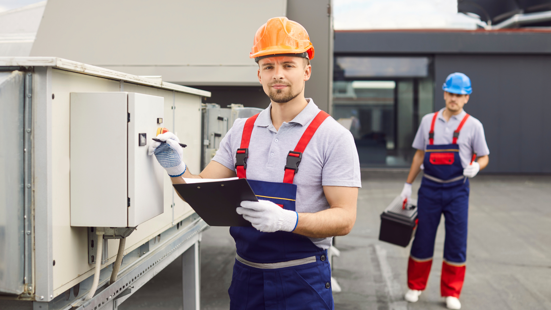 A man is holding a clipboard while another man is holding a toolbox.
