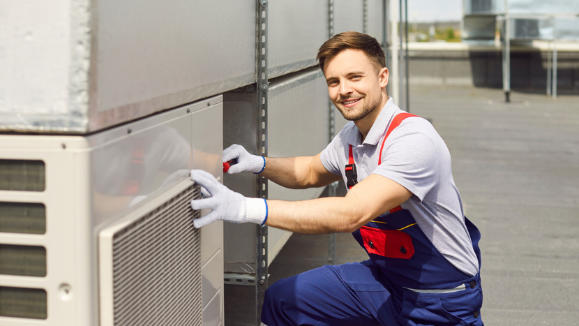 A man is kneeling down and working on an air conditioner.
