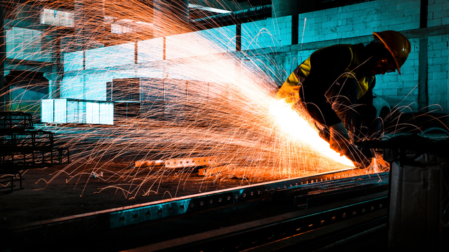 A man is cutting a piece of metal with a grinder in a factory.