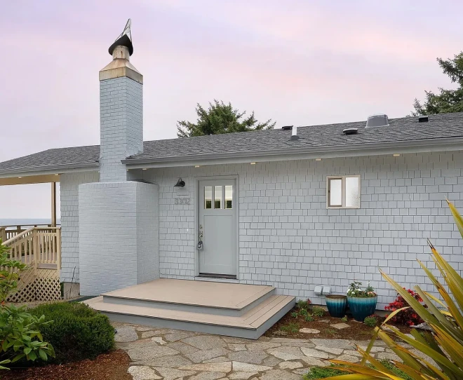 Gray house exterior with small porch, chimney, and stone walkway at dusk