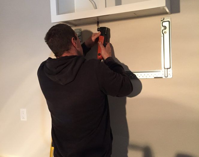 Person drilling a wall to mount a TV bracket above a fireplace in a living room