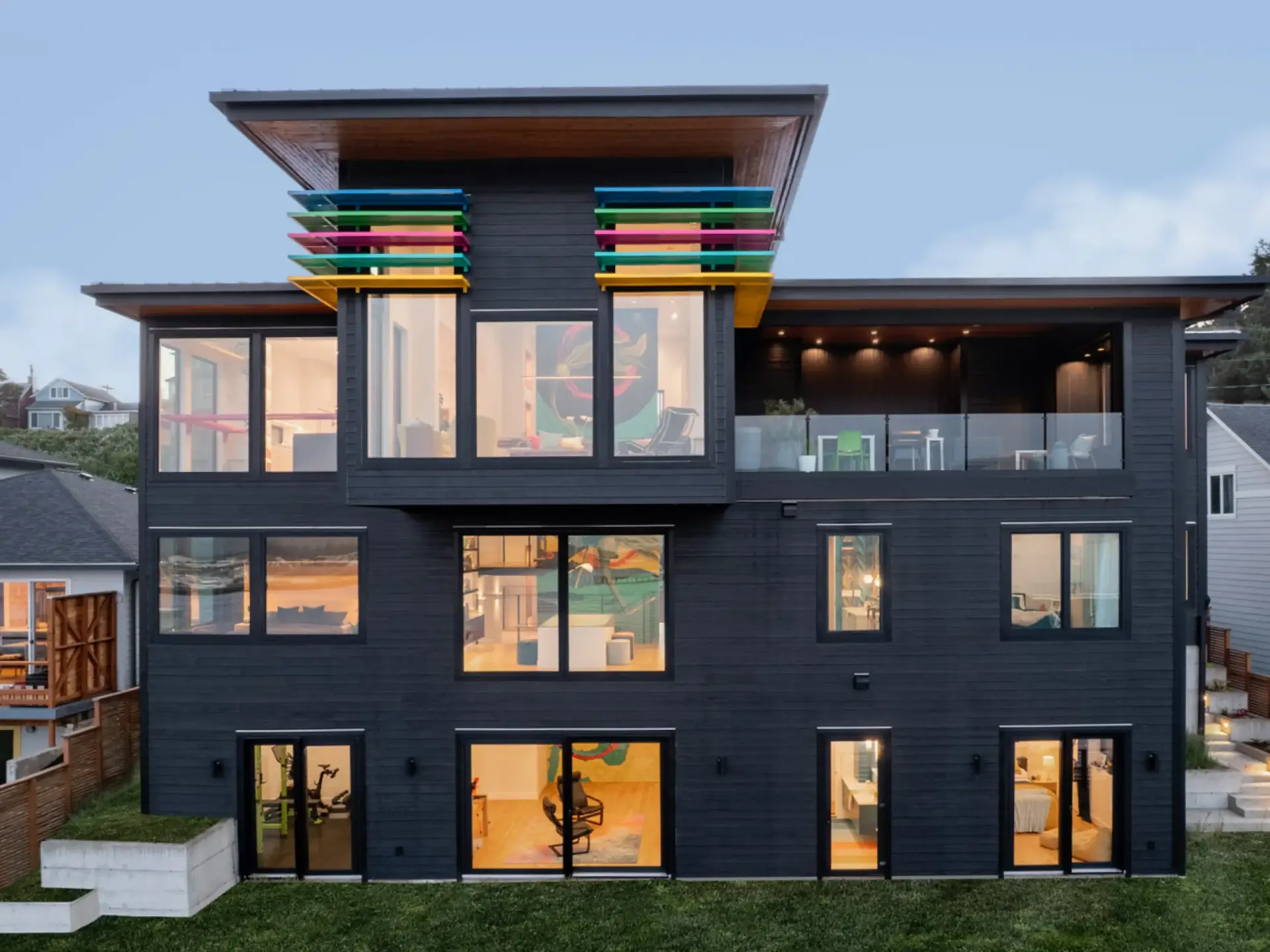 Modern black three-story house with colorful balcony slats at dusk