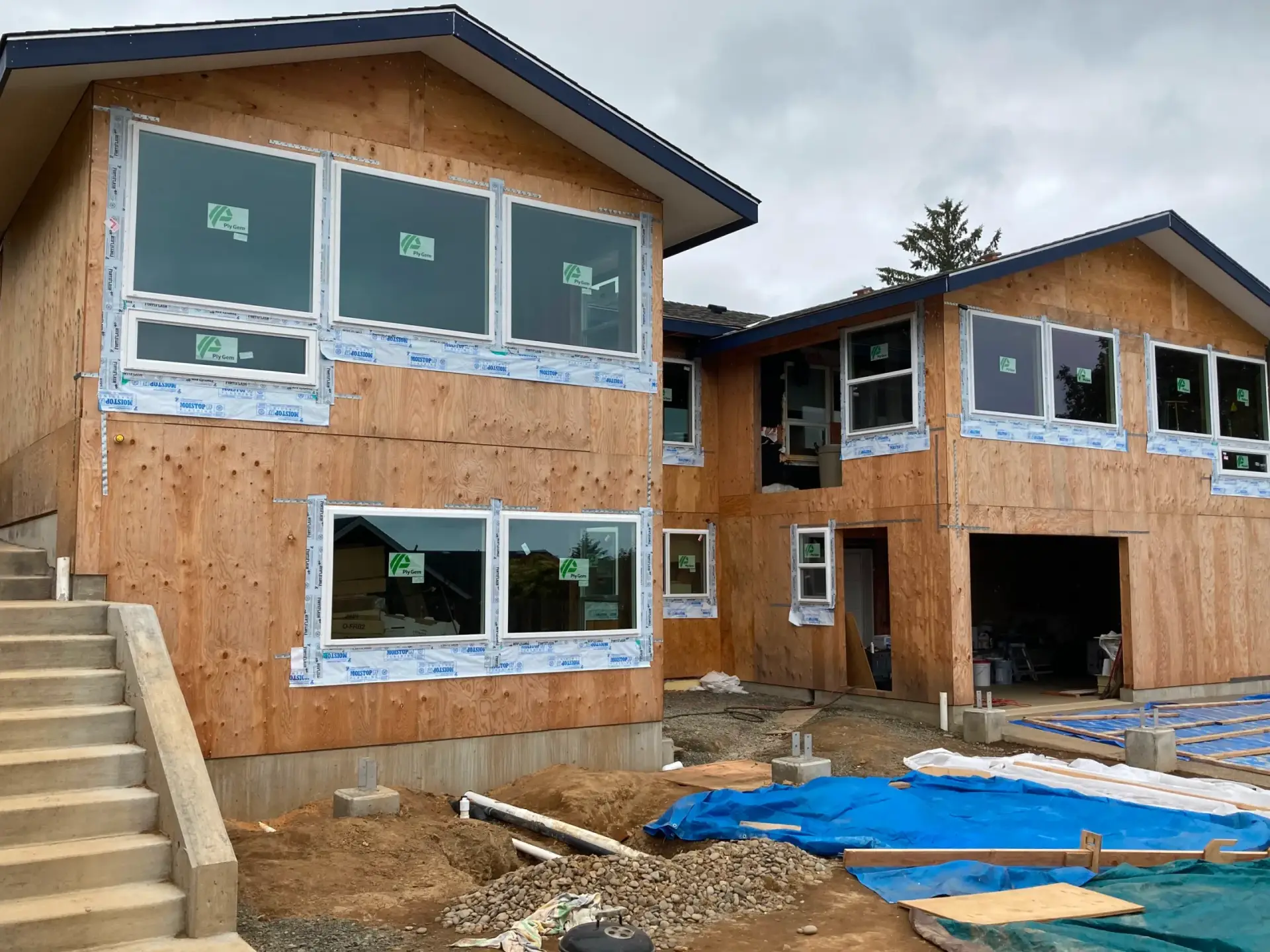 Newly framed house under construction with plywood exterior and blue tarps in front
