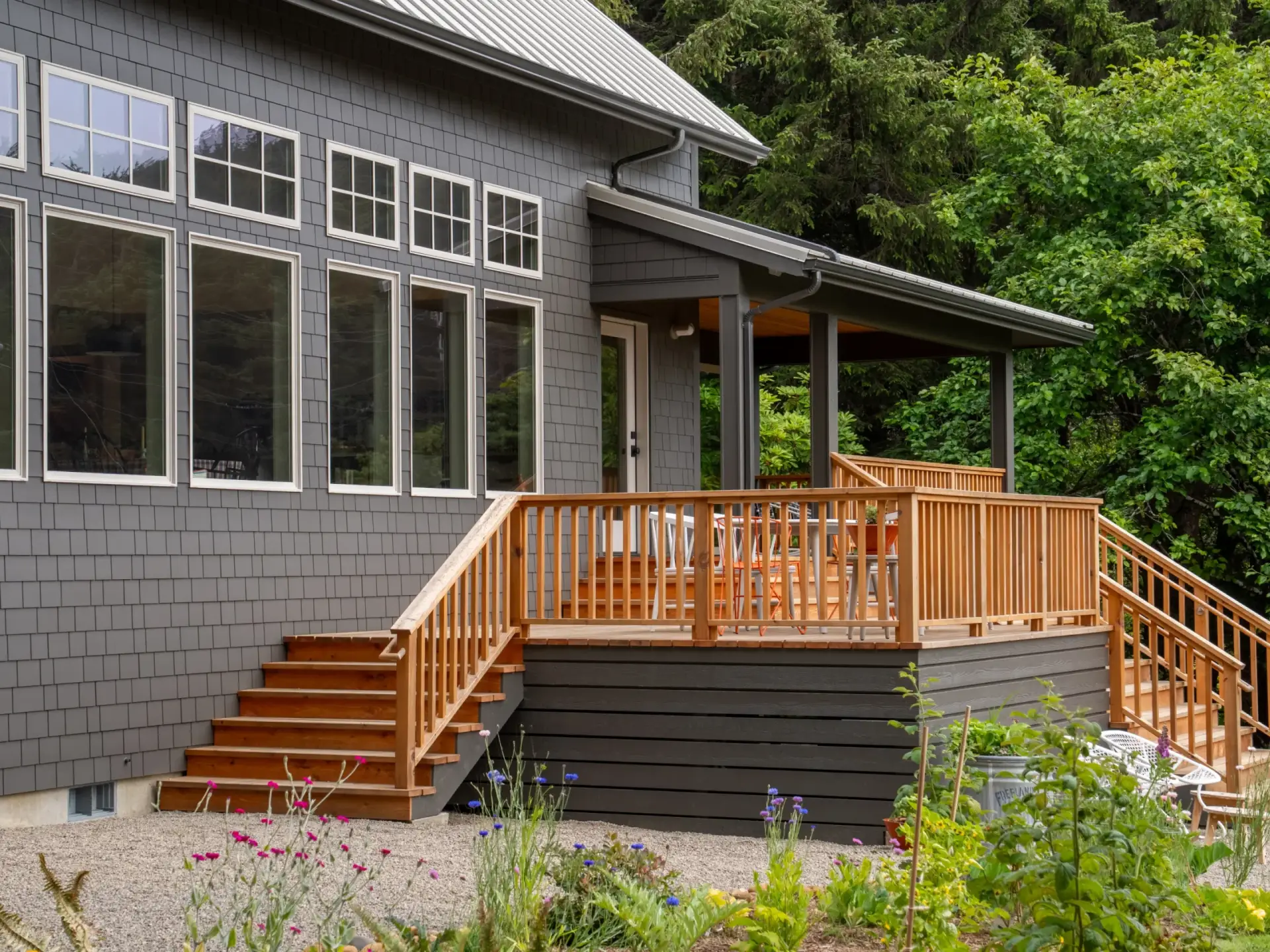 Wooden deck with railings on a gray house beside a wooded hillside