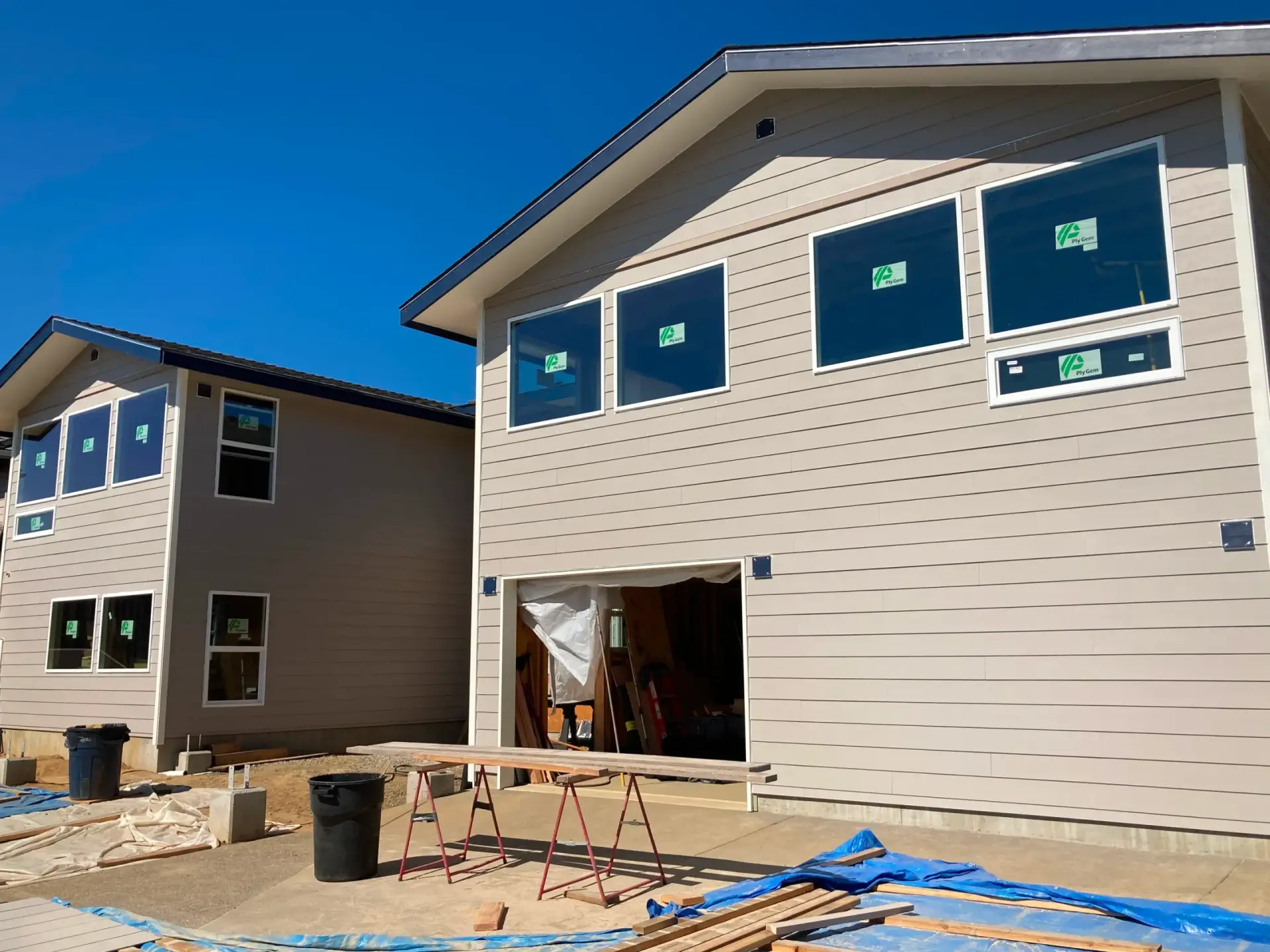 Two unfinished modern houses under construction with blue sky and exposed framing