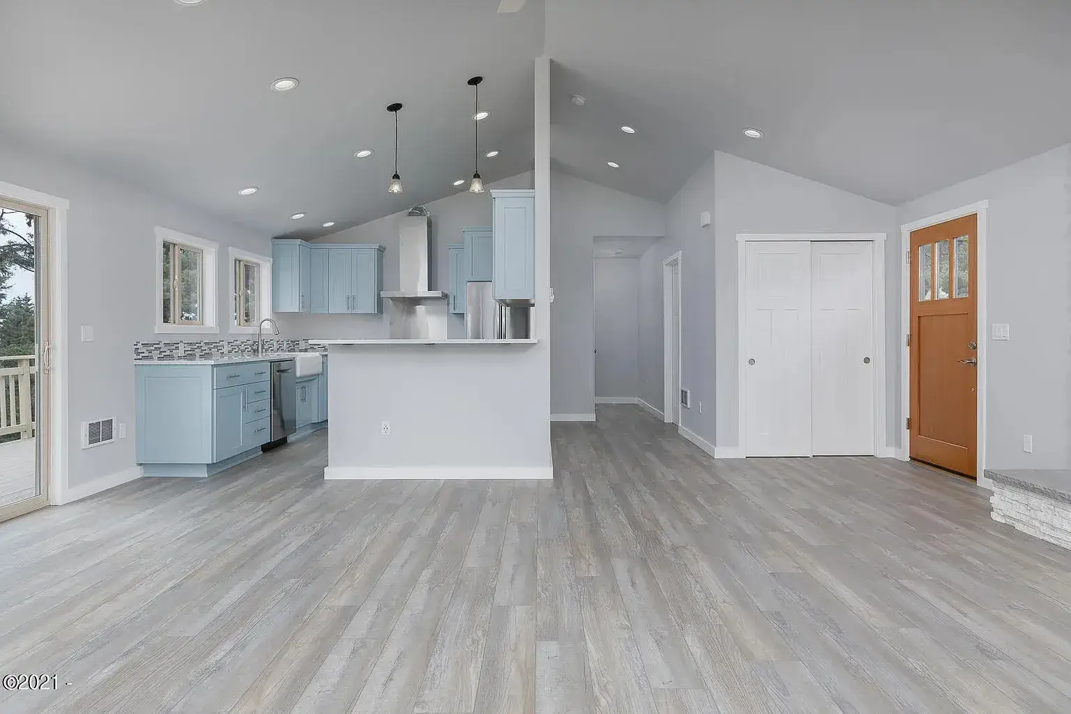 Bright empty modern kitchen and living area with light wood floors, white walls, and recessed lighting