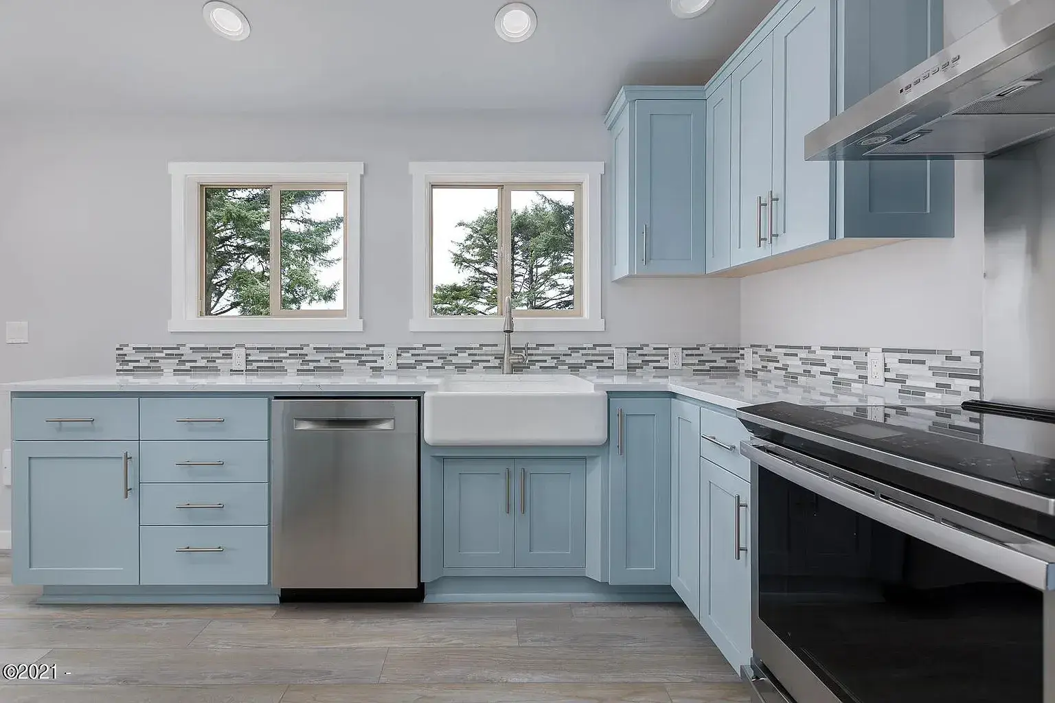Light blue kitchen with stainless steel appliances, white countertops, and mosaic tile backsplash
