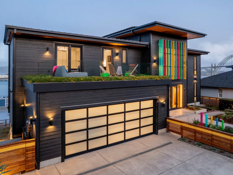 Modern two-story house with a lit garage and colorful vertical window accents at dusk