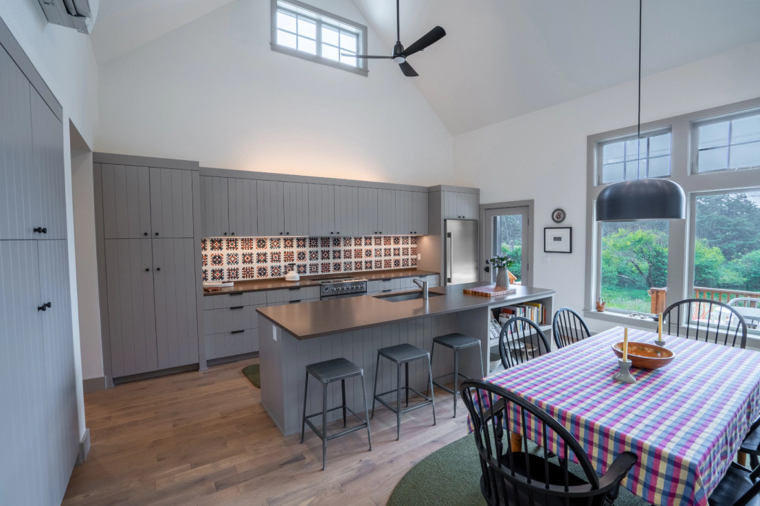 Bright open kitchen and dining area with gray cabinets, wood island, checkered tablecloth, and large windows