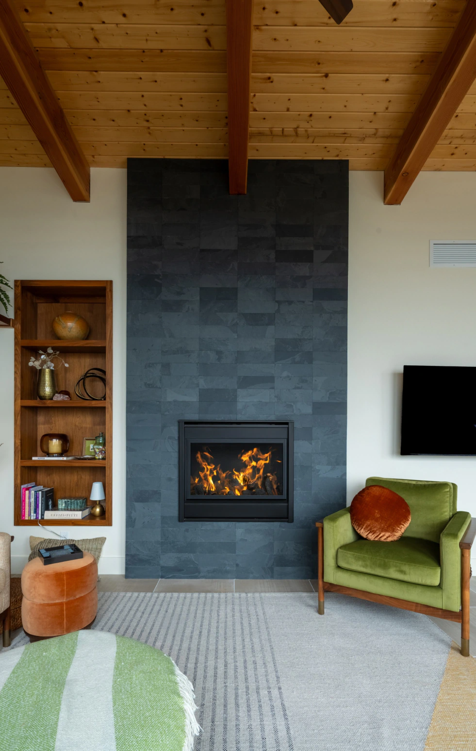 Cozy living room with a dark stone fireplace, green armchair, wood beams, and a lit fire.