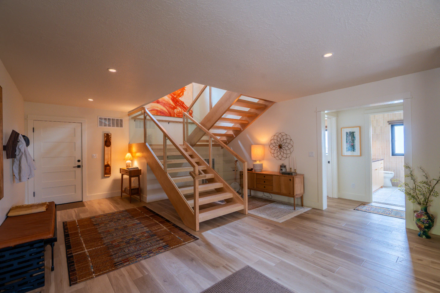 Bright modern foyer with staircase, hardwood floors, rug, lamp, and doors to adjoining rooms