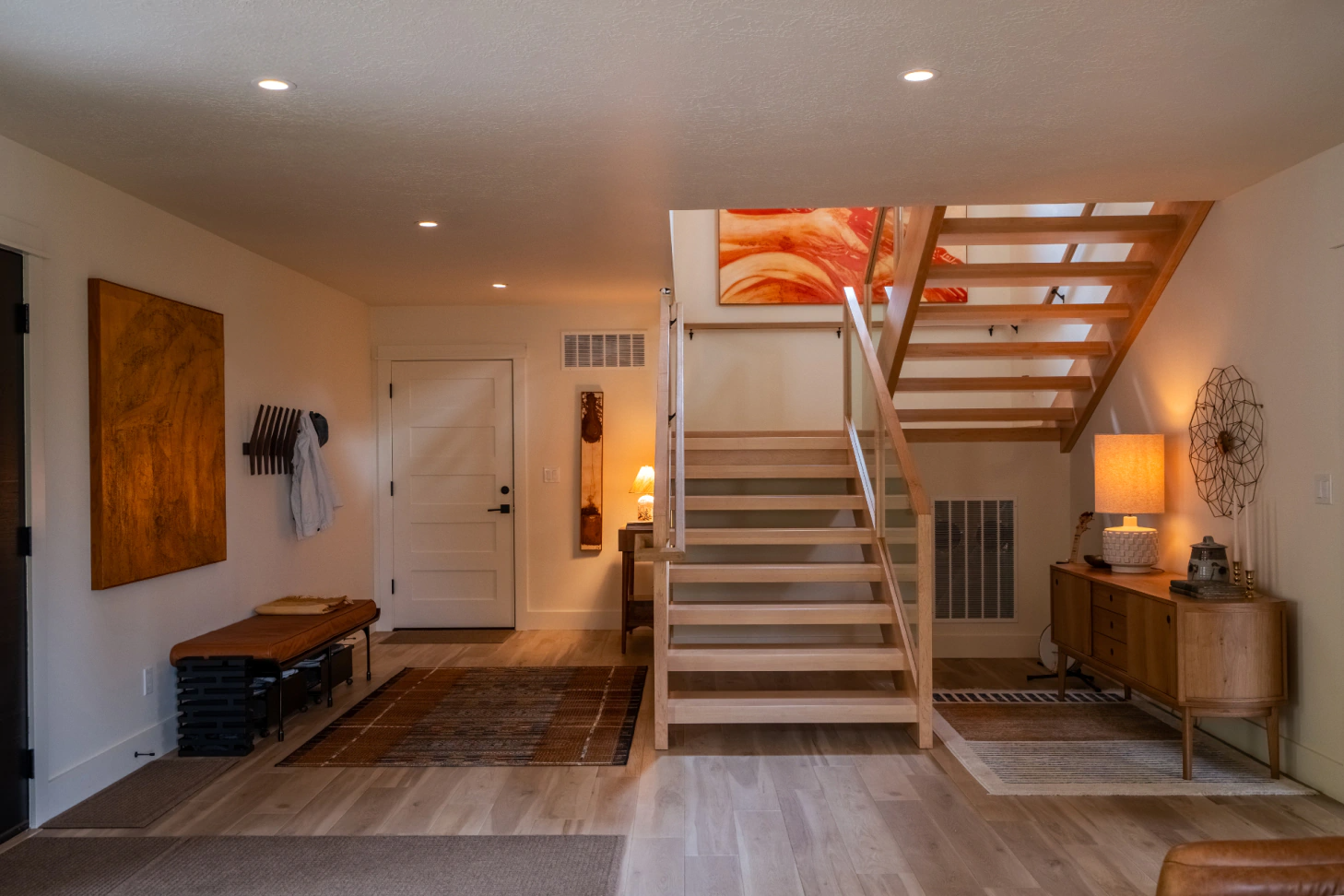 Modern hallway with staircase, white door, patterned runner, and warm wood accents in a well-lit home.