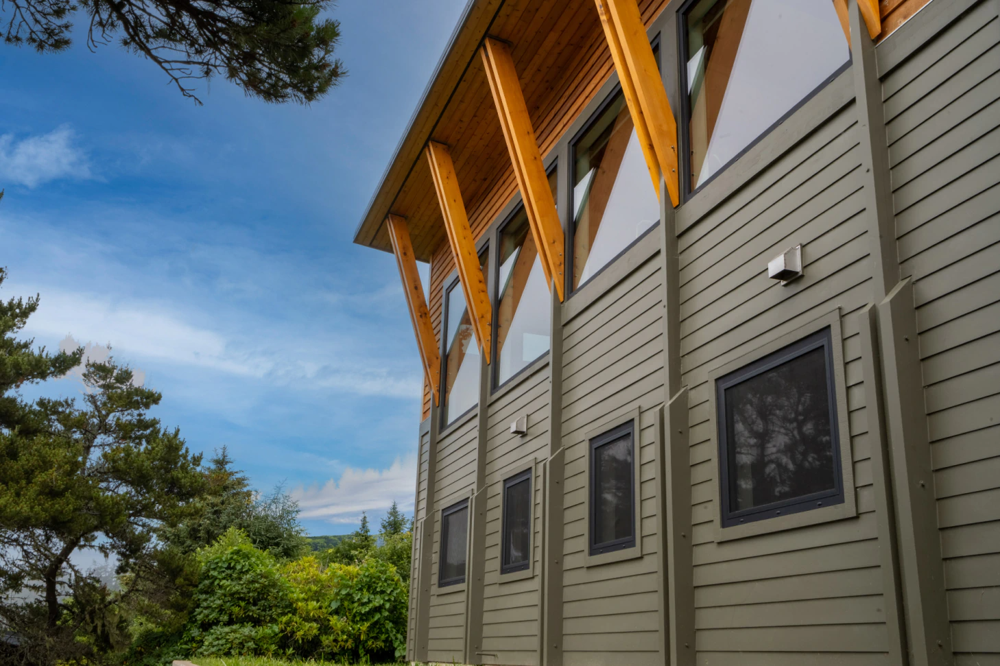 Modern building exterior with gray siding and orange wooden roof beams under a blue sky