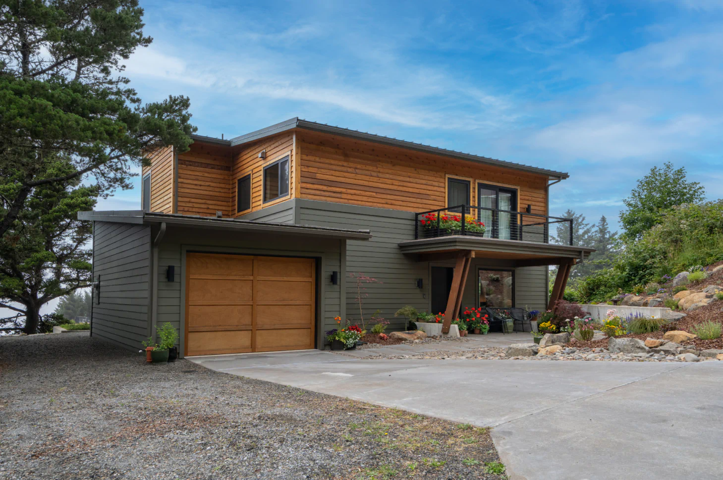 Modern two-story house with wood siding, garage, and landscaped driveway under a blue sky