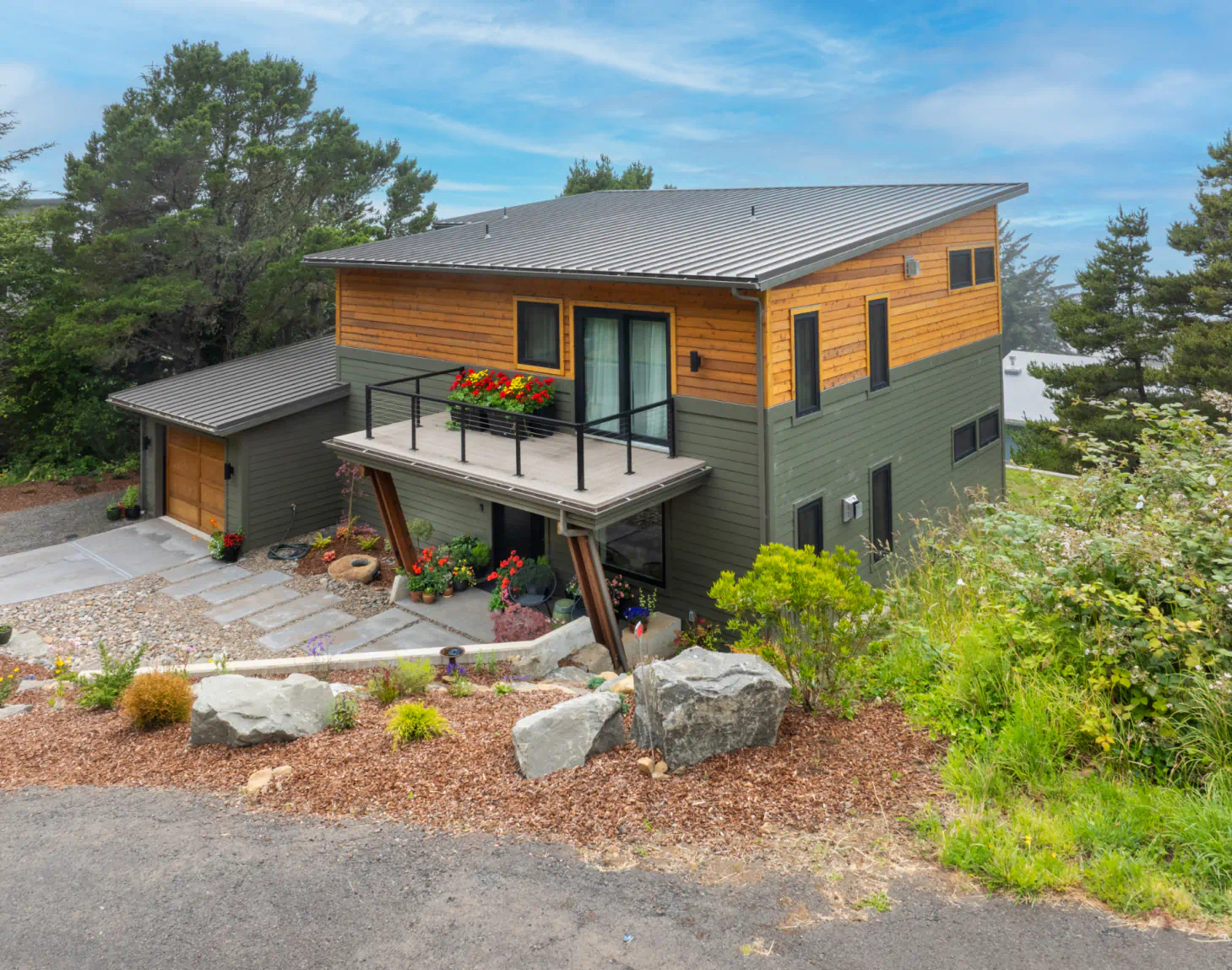 Modern two-story house with wood and dark siding, balcony, and landscaped hillside setting