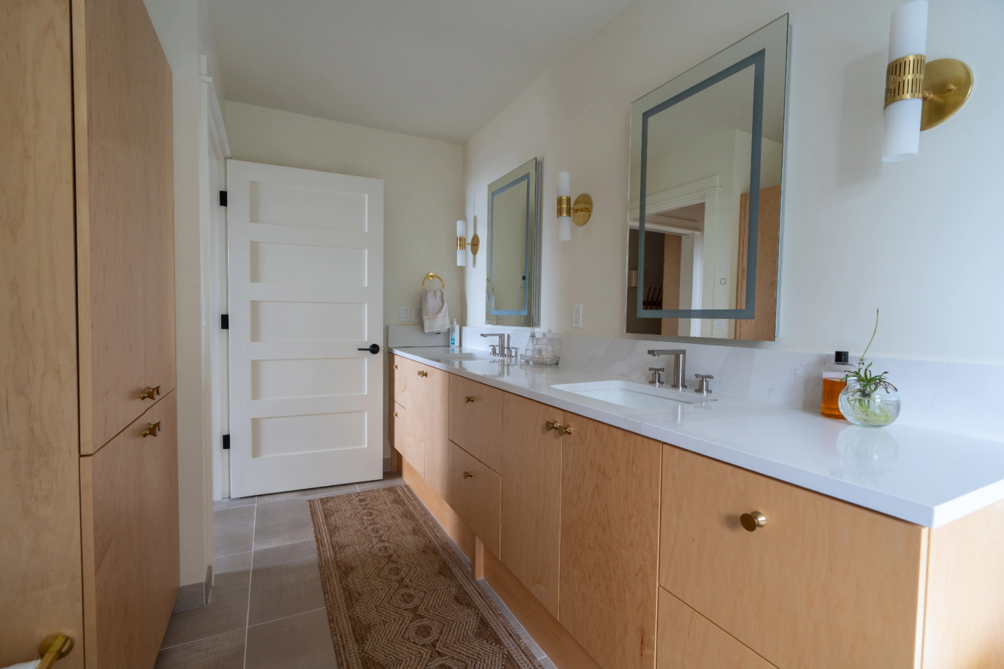 Bright bathroom with wood vanity, white countertop, mirror, sink, and woven runner rug