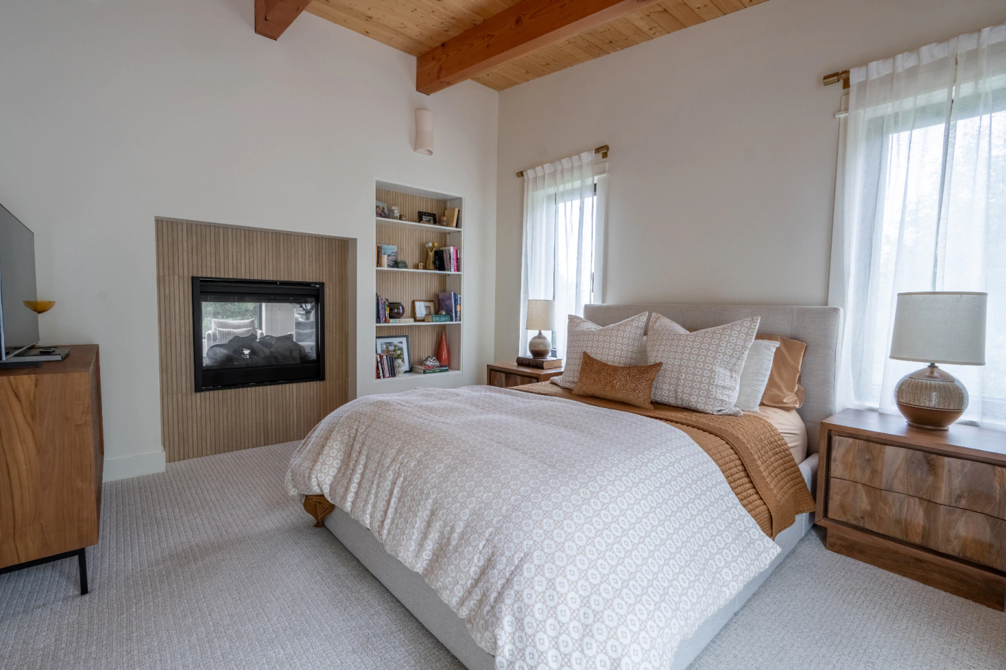Cozy bedroom with bed, fireplace, dresser, and two windows with sheer curtains