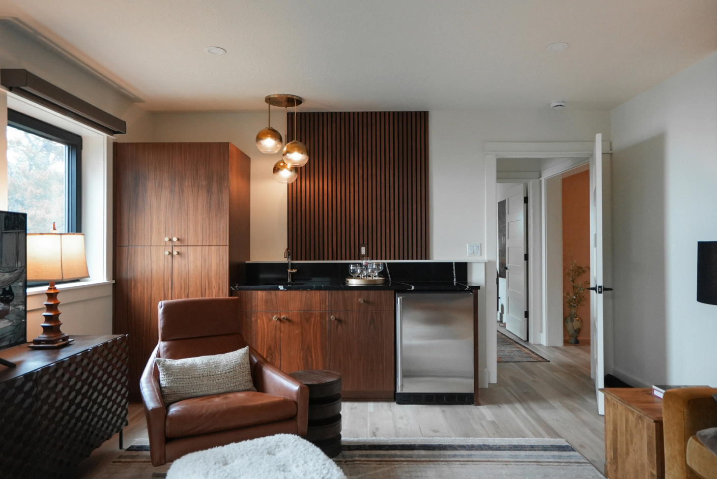 Modern living room and kitchen with wood cabinetry, black countertops, and a leather chair near a window.