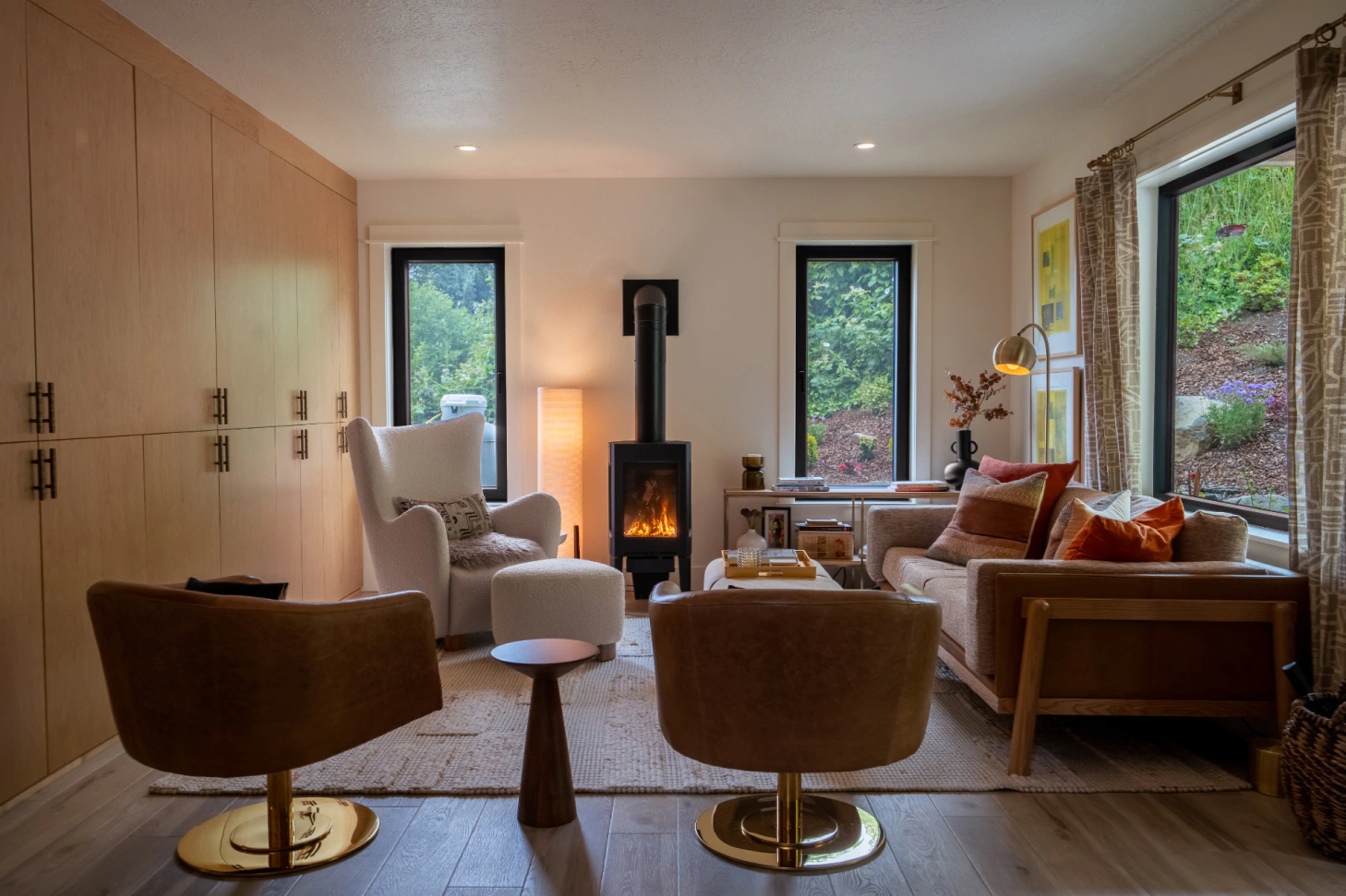 Cozy living room with fireplace, armchairs, sofa, and large windows overlooking greenery