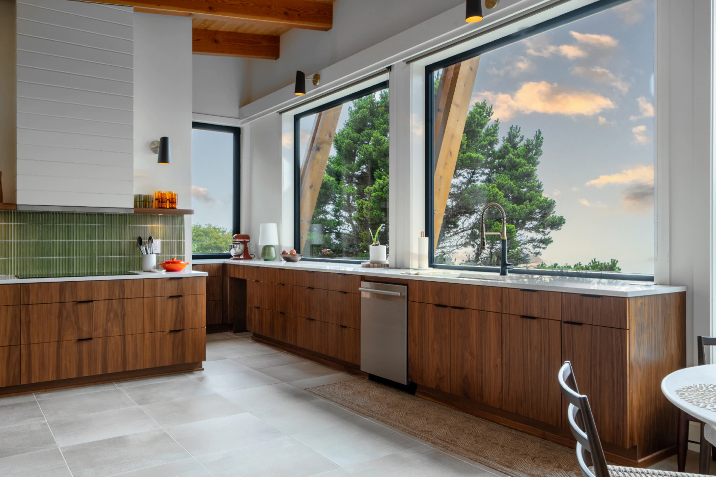 Modern kitchen with wood cabinets, white tile walls, and large windows overlooking trees and sky