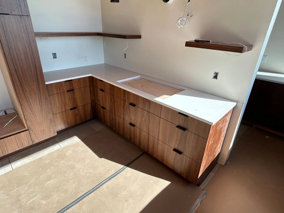 Built-in wooden kitchen cabinets with white countertops and wall shelves in a bright room