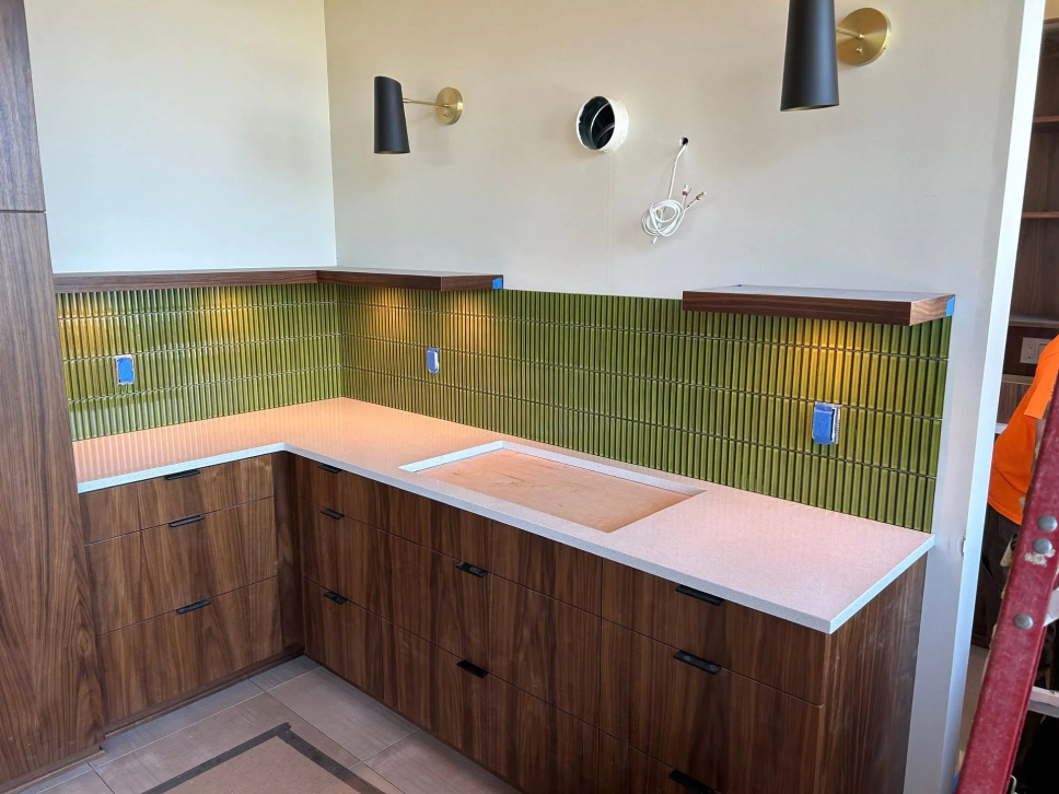 L-shaped kitchen countertop with wood cabinets, white surface, and green tile backsplash under wall sconces