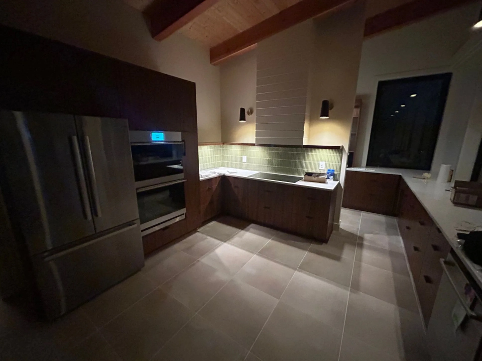 Modern kitchen with stainless steel appliances, dark wood cabinets, beige tile floor, and a lit backsplash
