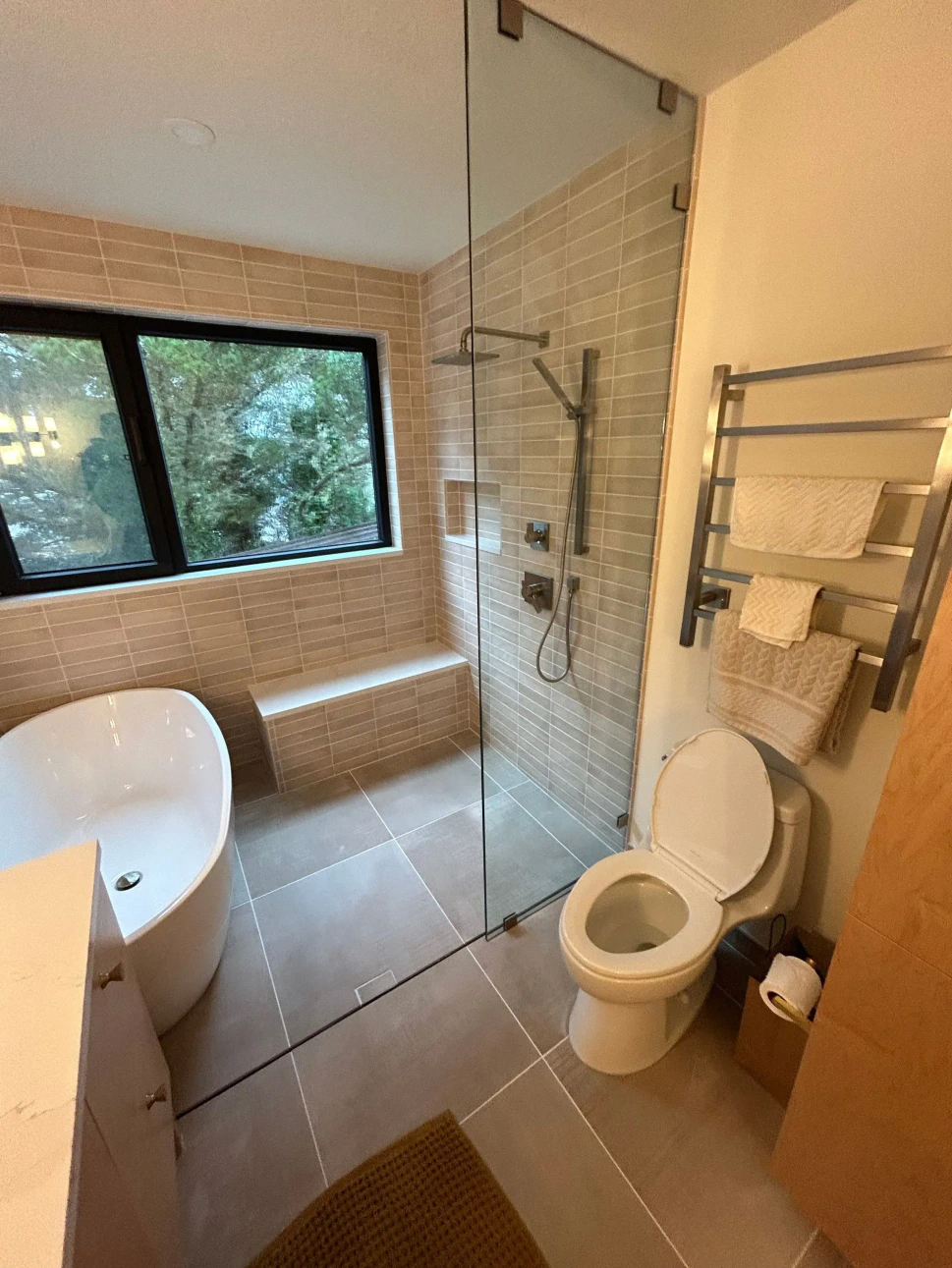Small bathroom with a bathtub, toilet, shower, towel rack, and window.
