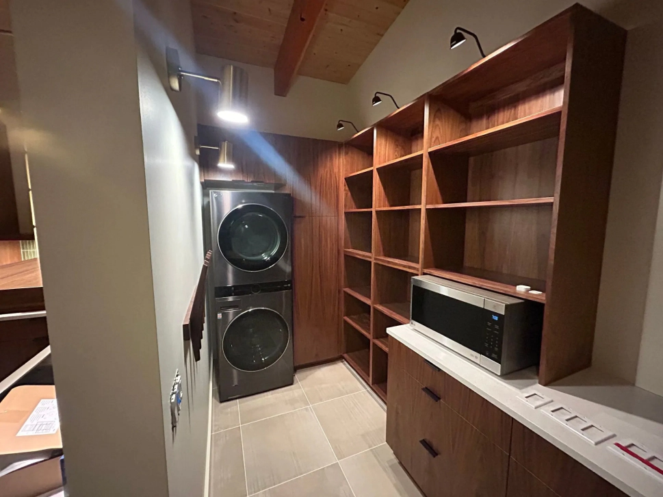 Narrow hallway with built-in wooden shelves, a countertop, and stacked washer and dryer under slanted ceiling.