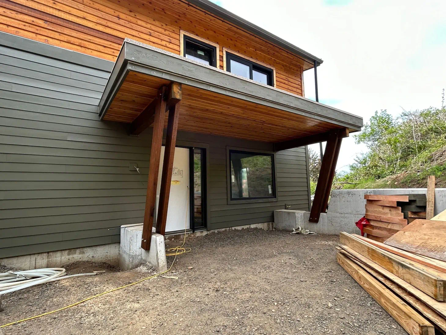 Modern house exterior with covered entry, wood siding, and gravel driveway