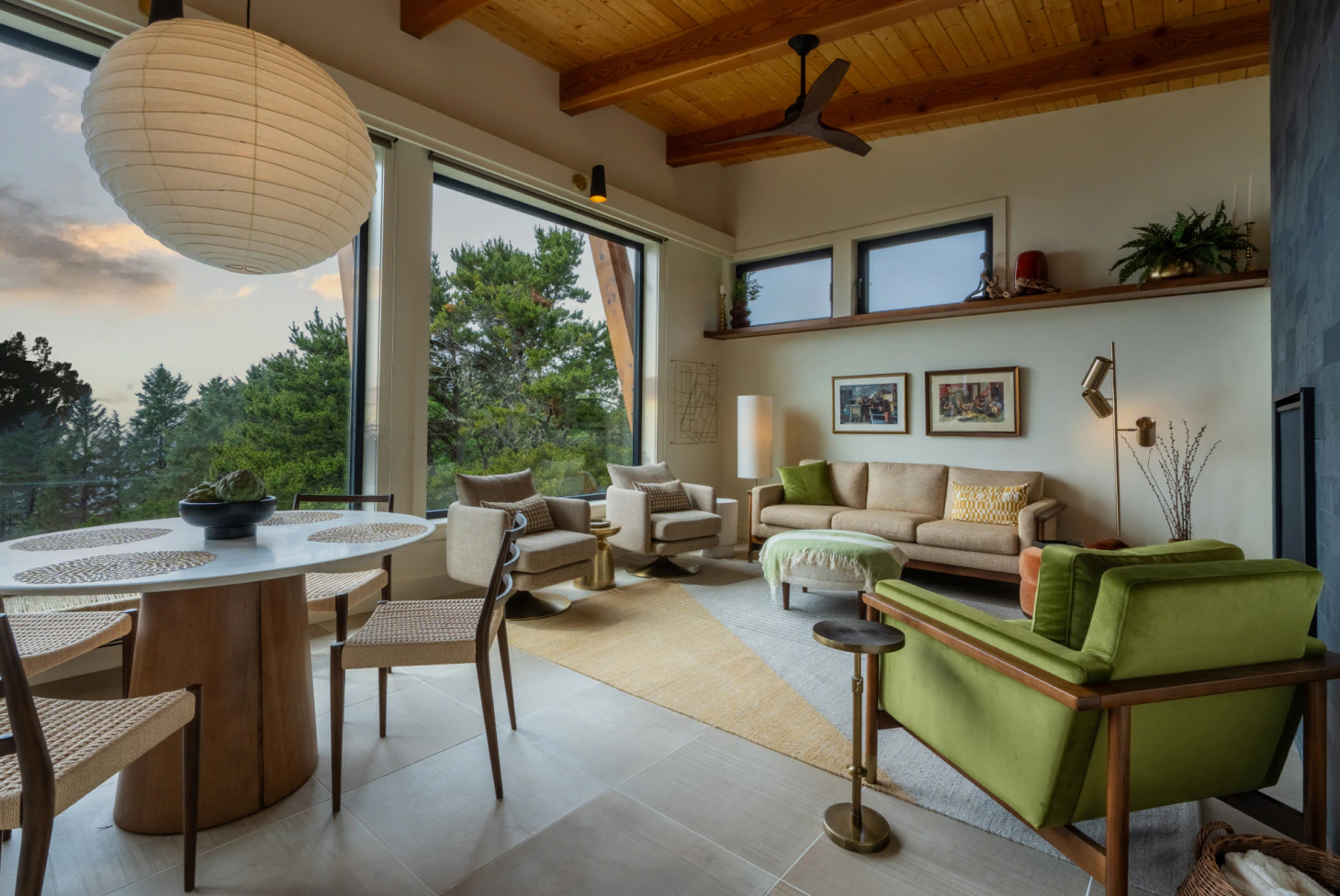 Modern living room with large windows, beige sofa, green armchair, and wooden ceiling