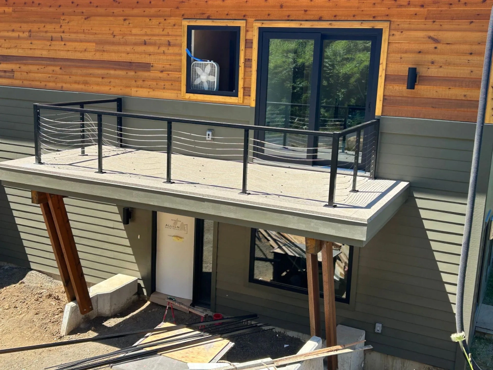 Modern house exterior with wooden siding, upper deck, black railings, and a basement entrance beneath