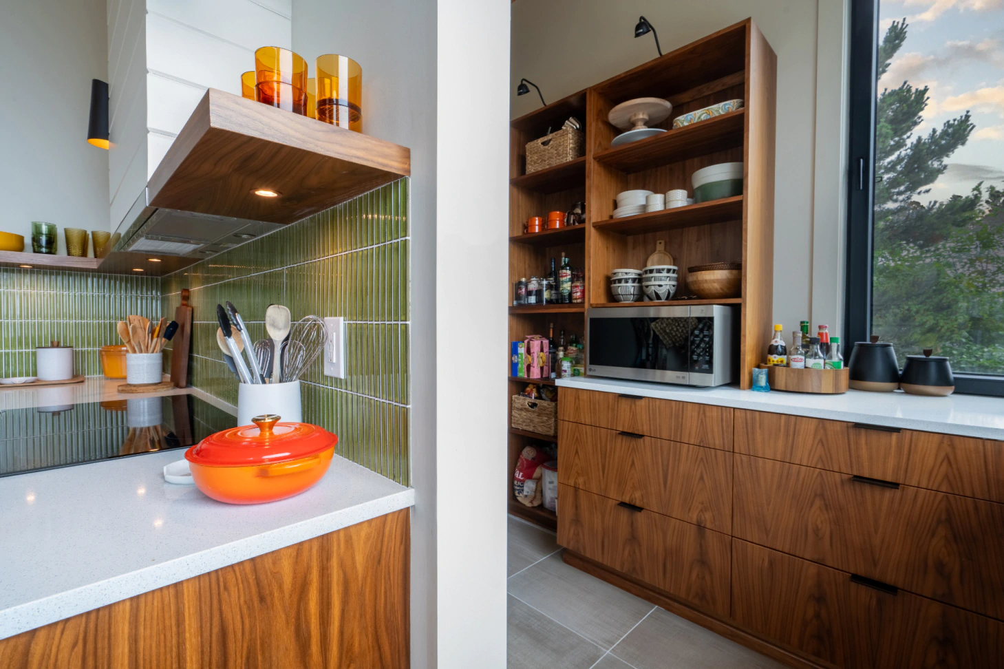 Modern kitchen with green tile backsplash, wood cabinets, shelves, and an orange bowl on the counter