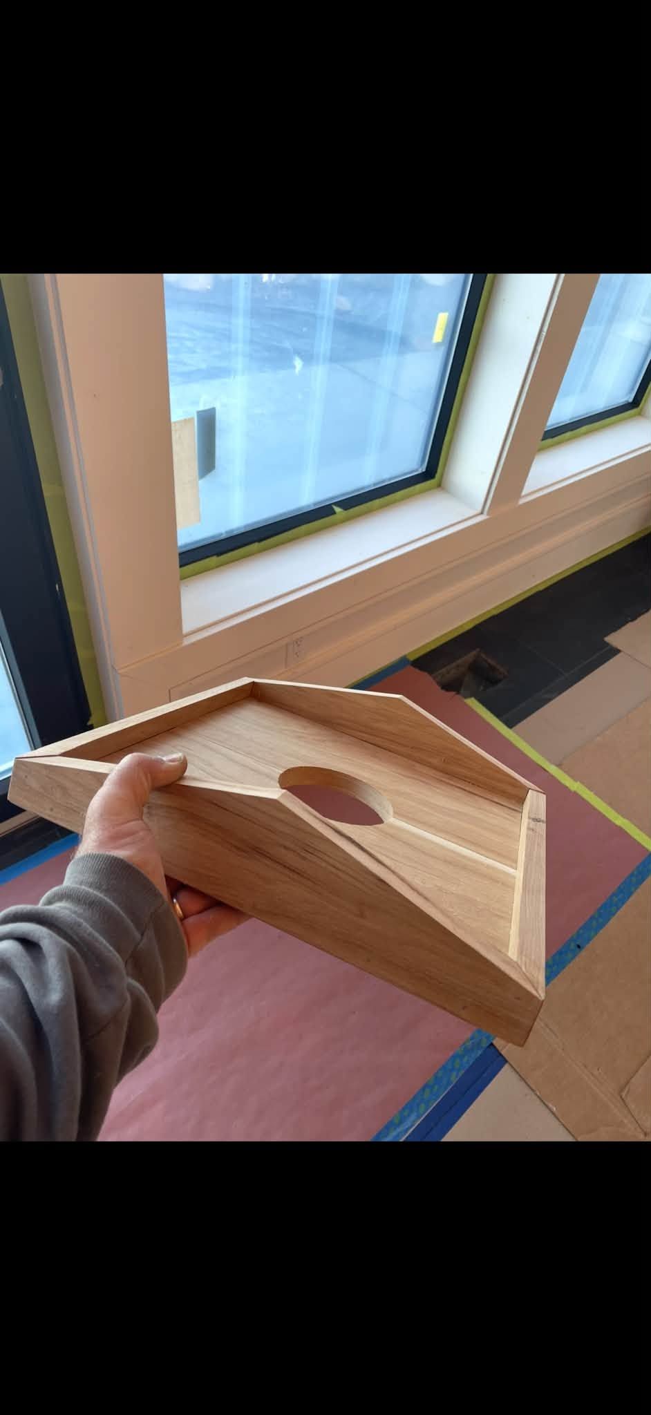 Person holding a wooden triangular object by a sunny window.