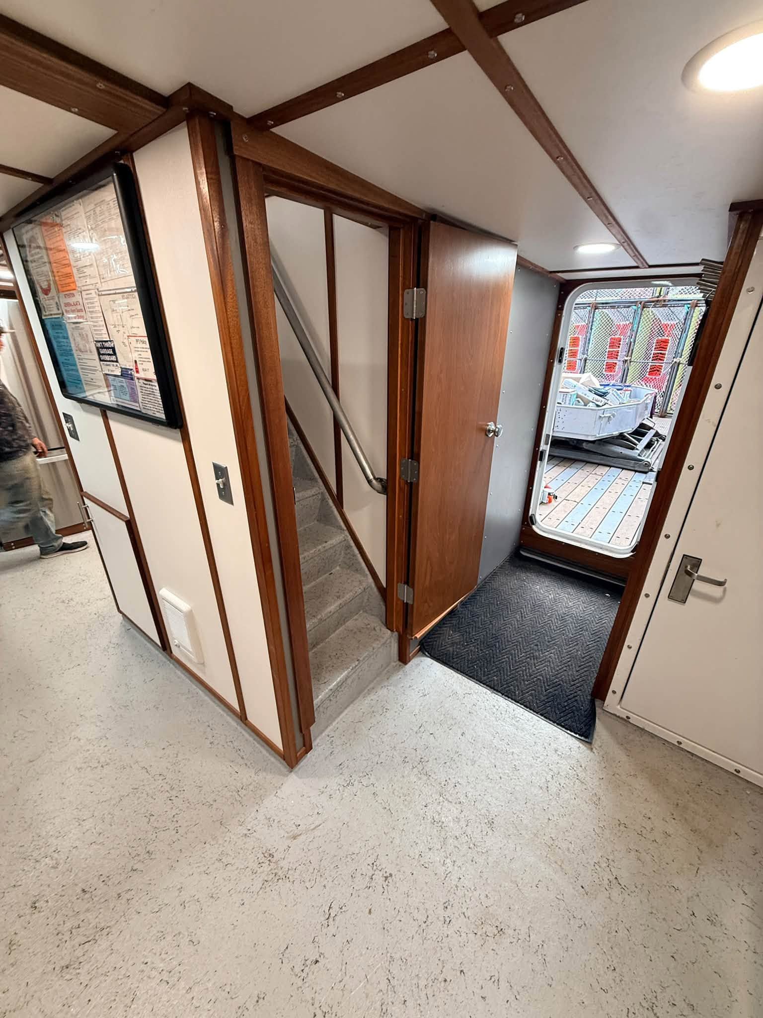 Hallway with wood-framed partitions, white walls, speckled floor, and a door opening to a brighter room