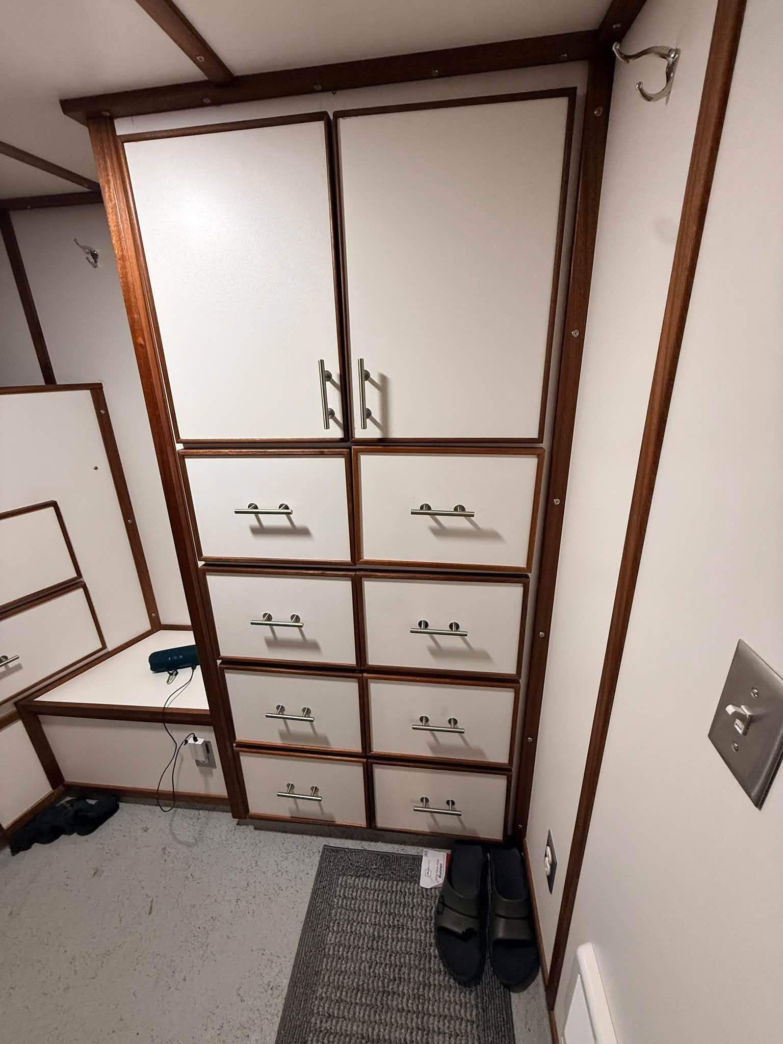 Small room with built-in white storage cabinets, drawers, and hanging clothes, viewed from the doorway.