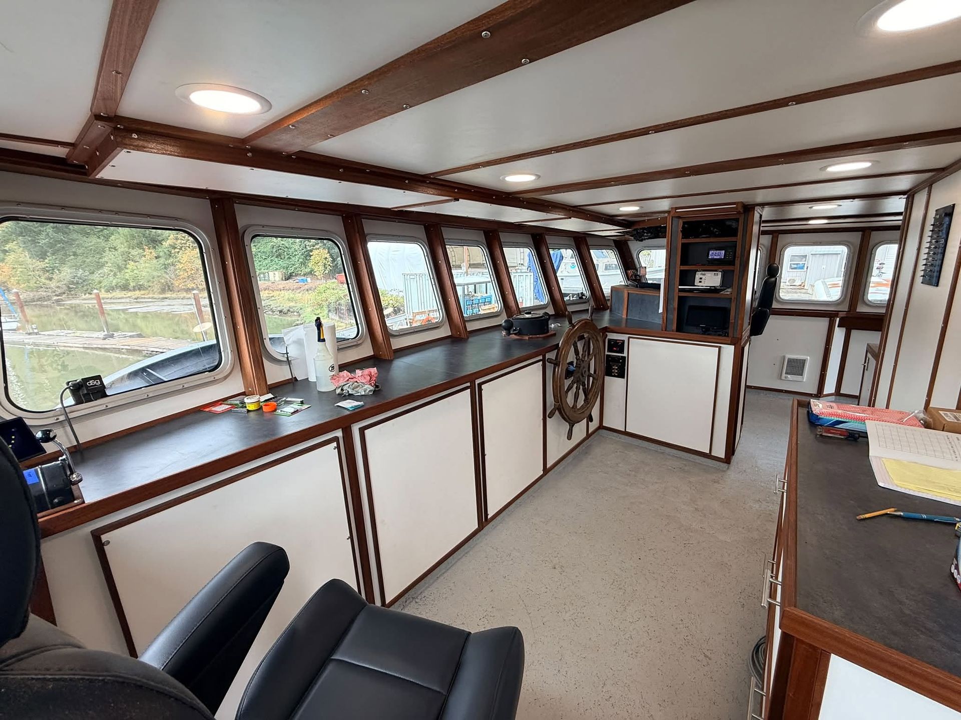 Interior of a boat cabin with large windows, white cabinets, and a carpeted floor, viewed from the helm.