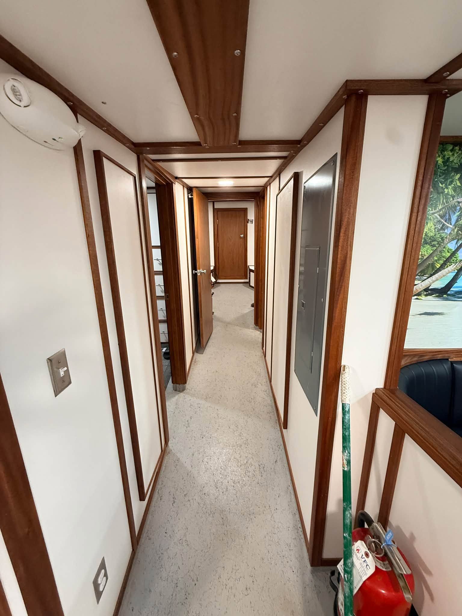 Narrow carpeted hallway with wood trim and doors, leading to a brighter room at the end.