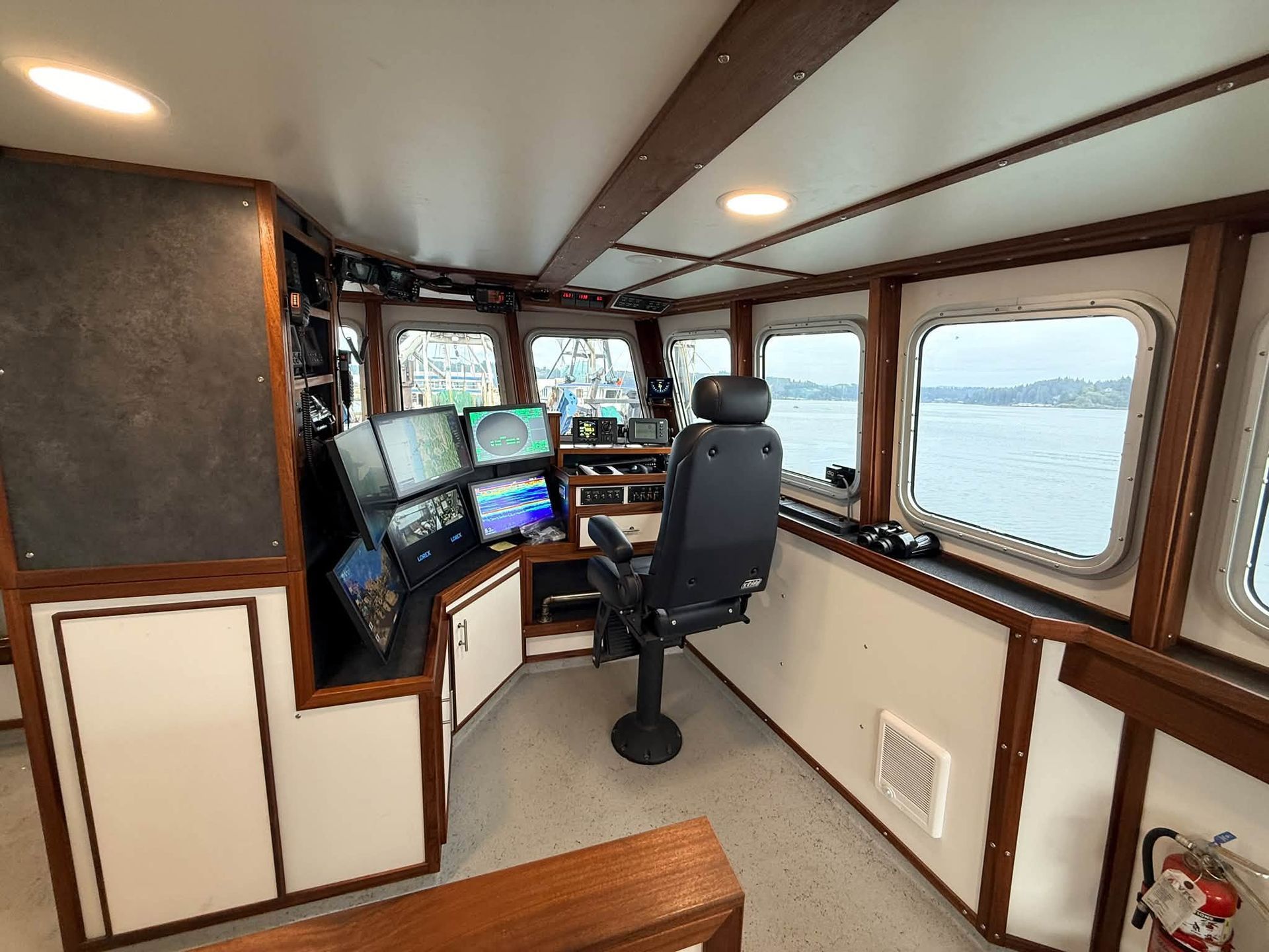 Compact boat helm with steering chair, control panels, and large windows overlooking the water.