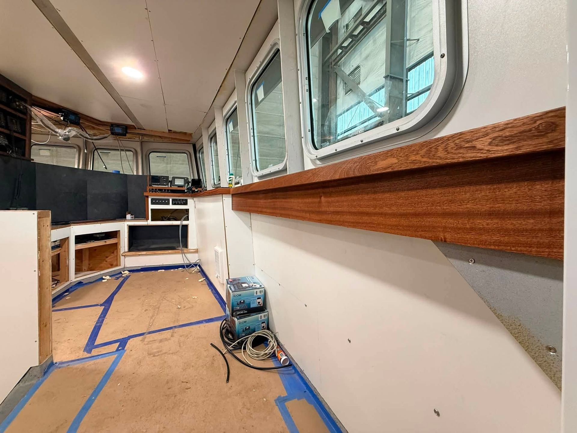 Partially renovated bus interior with taped floor, blue power tool, and wood trim along the windows
