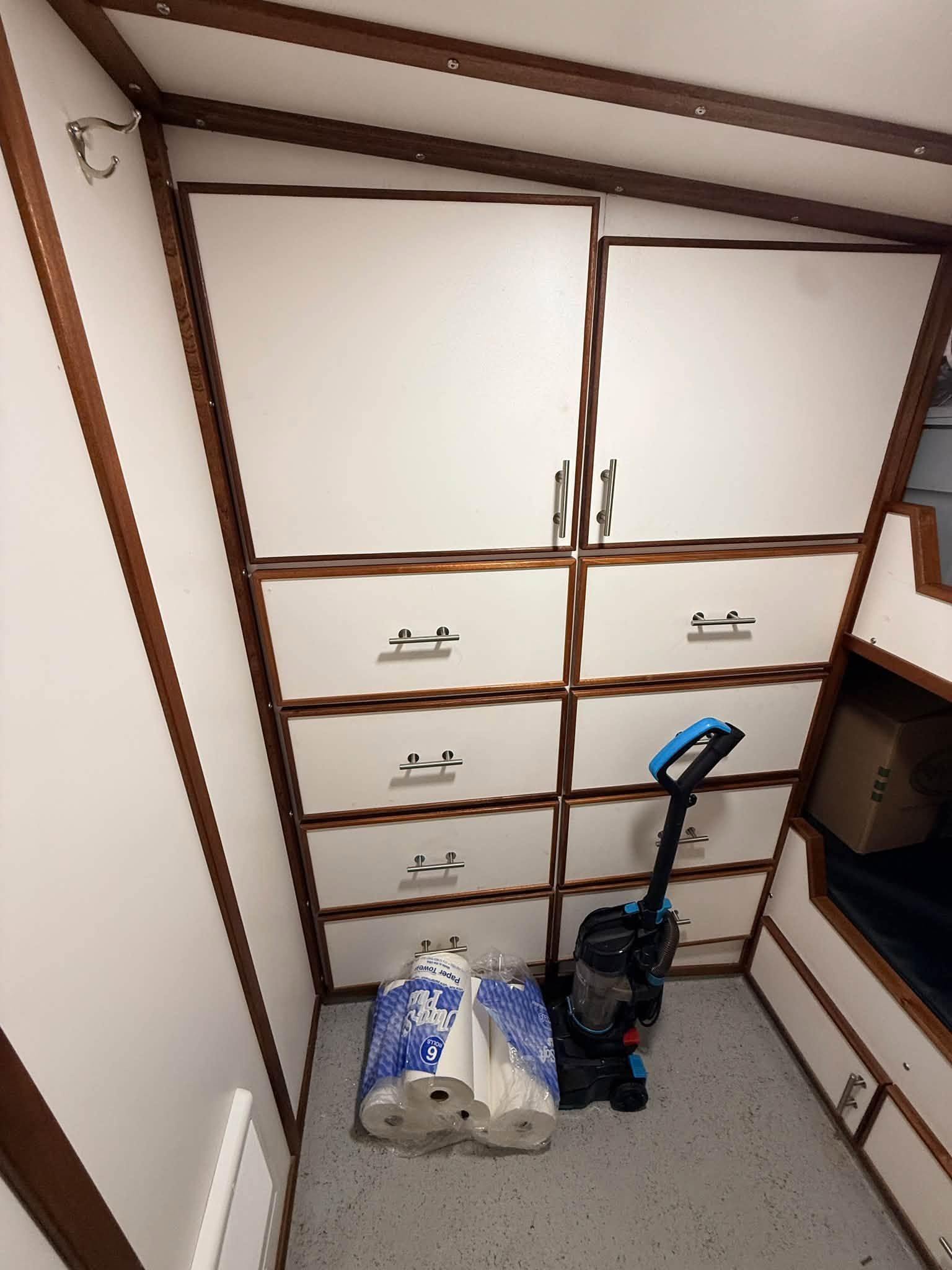 Small attic storage nook with white cabinets, a blue vacuum, and two bags on the floor.