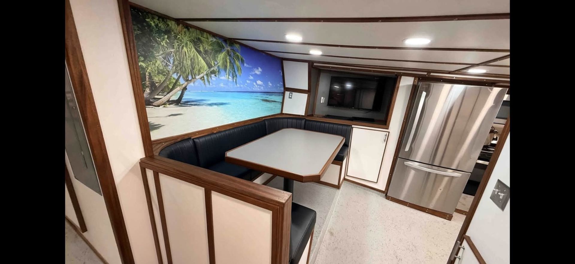 Compact RV kitchen with booth dining nook, beach mural, and stainless steel refrigerator