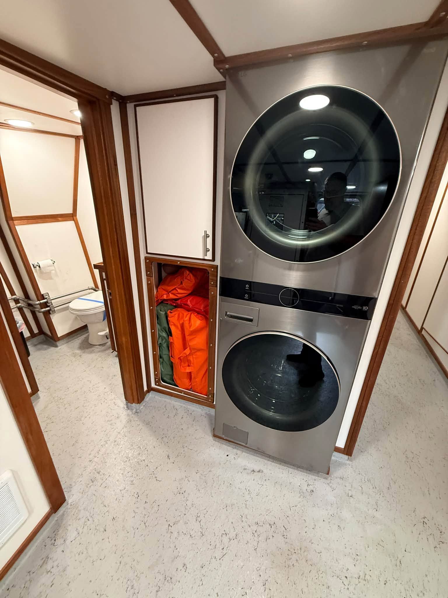 Stacked washer and dryer in a laundry nook, with an open lower door showing orange items inside.