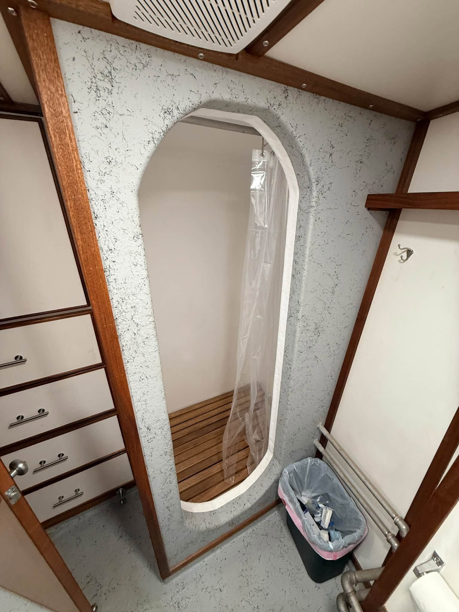 Narrow closet with an oval mirror, wood shelving, drawers, and a small trash bin on the floor.
