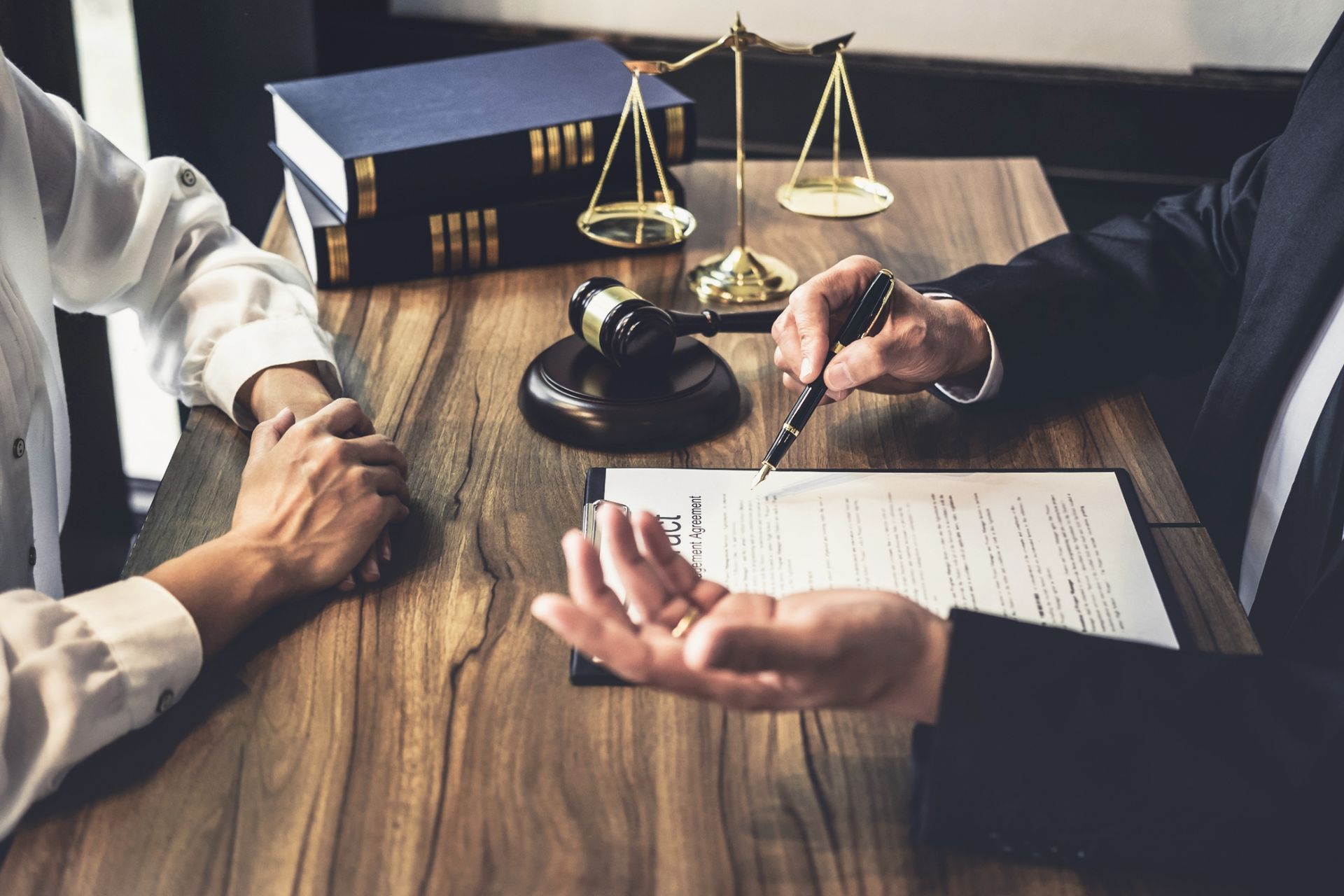 Lawyer and client signing documents at a desk with a judge’s gavel and scales of justice