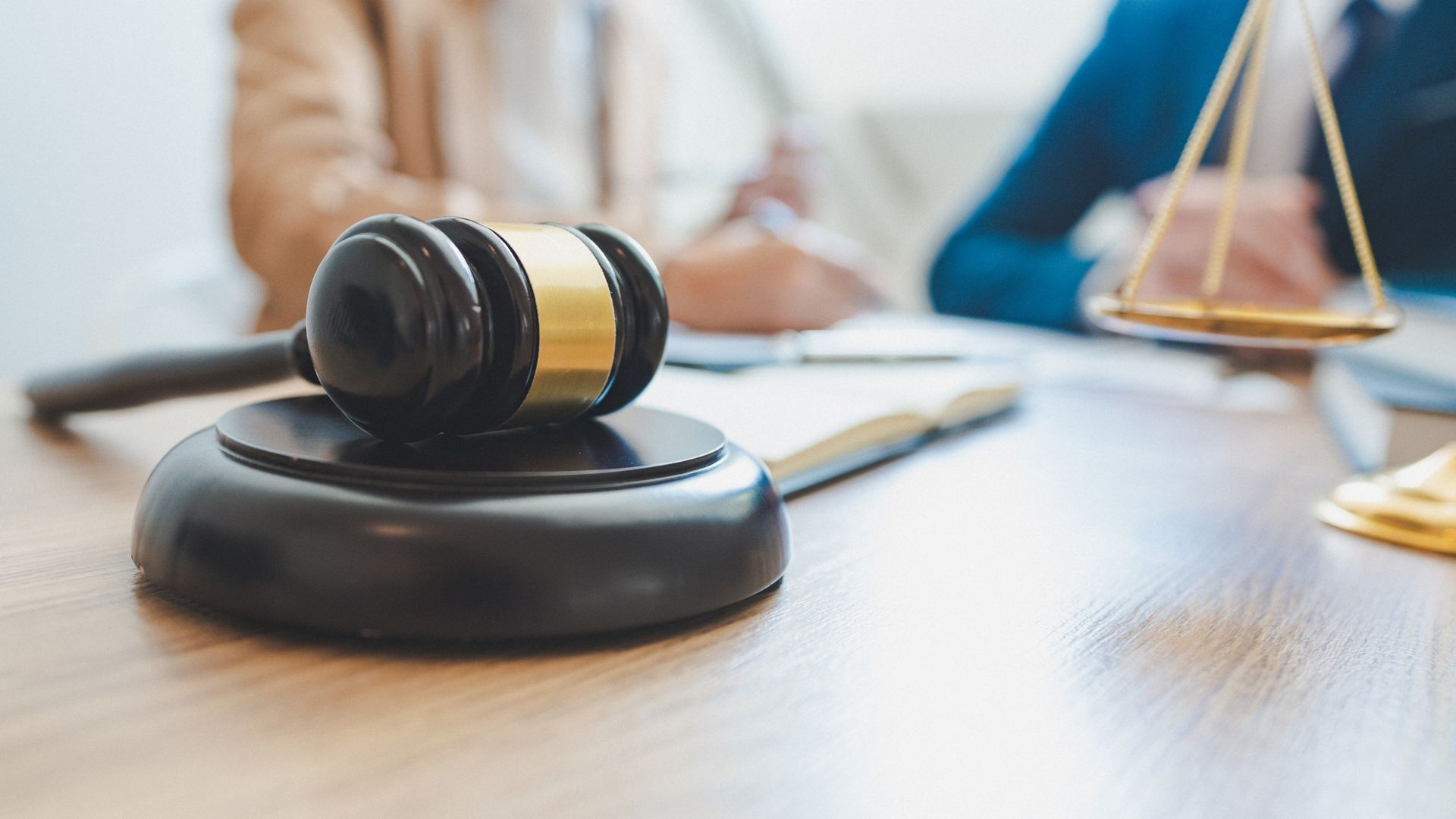 Judge’s gavel on a desk with a blurred lawyer and scales of justice in the background