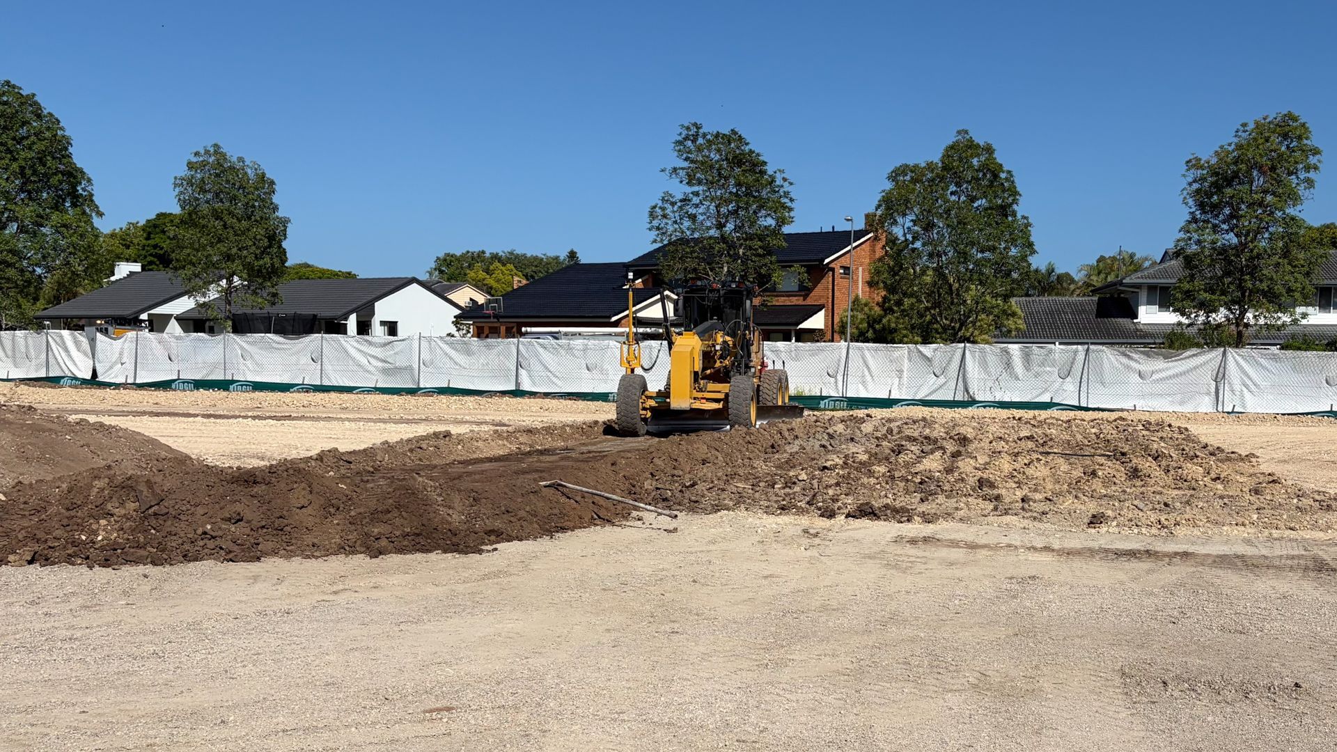 Blue excavator digging in a construction site with dirt and concrete blocks under a blue sky.
