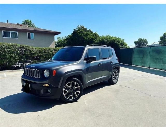Gray Jeep Renegade parked on a sunny driveway beside a house and green fence